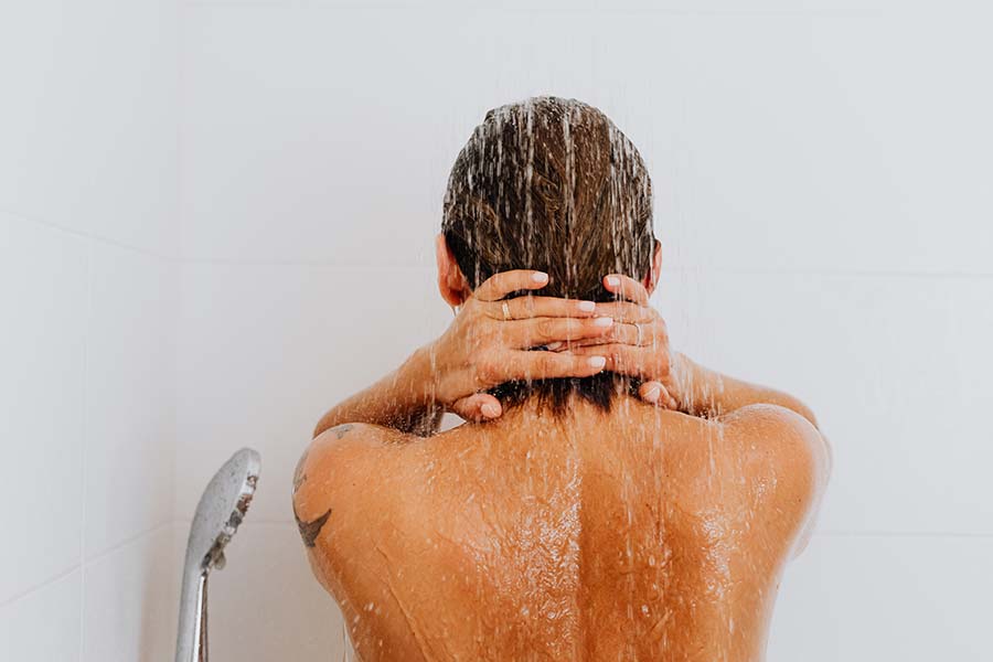 Kobieta z tatuażem na ramieniu, myjąca włosy pod prysznicem.